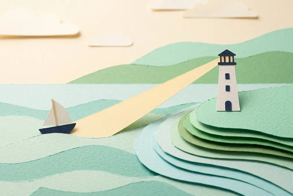 Paper-cutout diorama of a lighthouse on a headland casting a warm beam across a calm paper sea to guide a small sailboat safely across